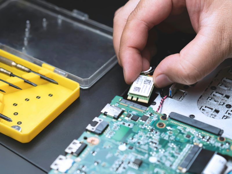 Technician's hand holding computer chip for install on electronic circuit motherboard of laptop