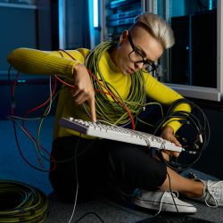 Young woman IT technician wrapped in wire repairing keyboard